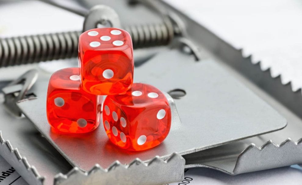 3 red dice on a mousetrap demonstrating the concept of gambling risk/scams.
