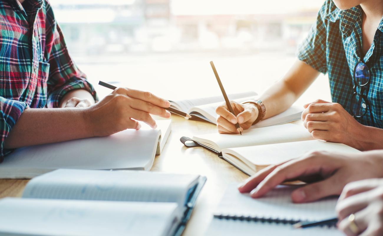 3 people studying with pencils and notepads on a wooden surface