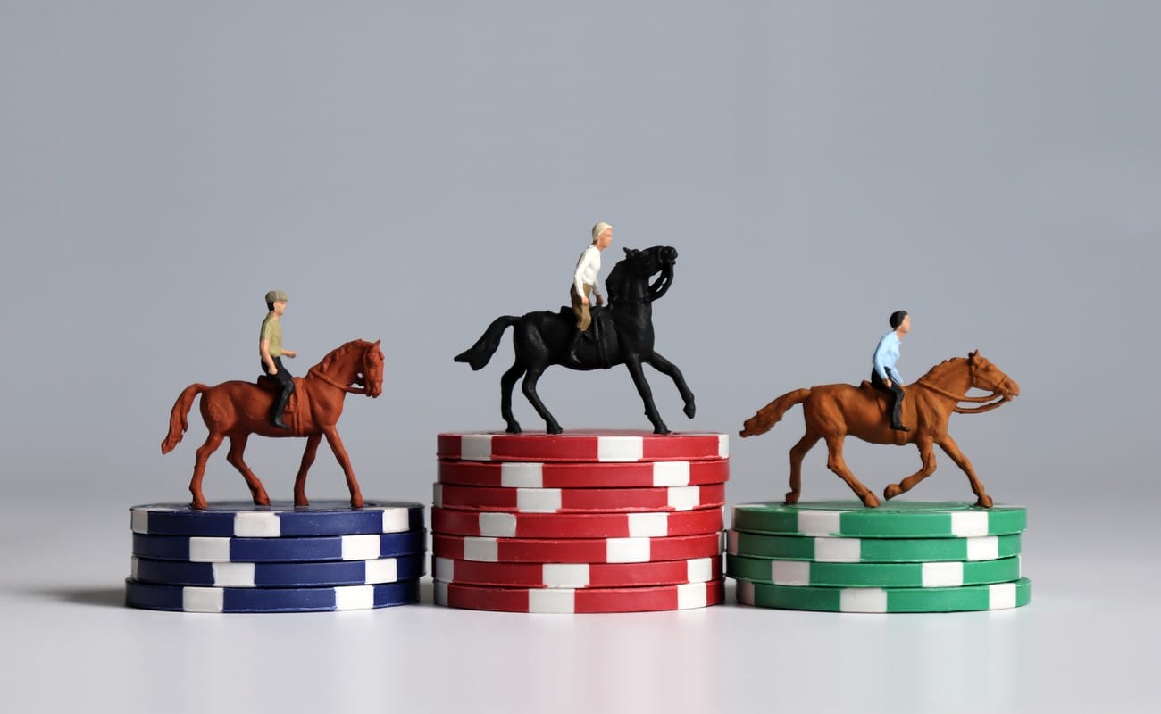 1 plastic toy brown horse and jockey on a stack of blue poker chips, 1 plastic toy black horse and jockey on a stack of red poker chips and 1 plastic toy brown horse and jockey on a stack of green poker chips