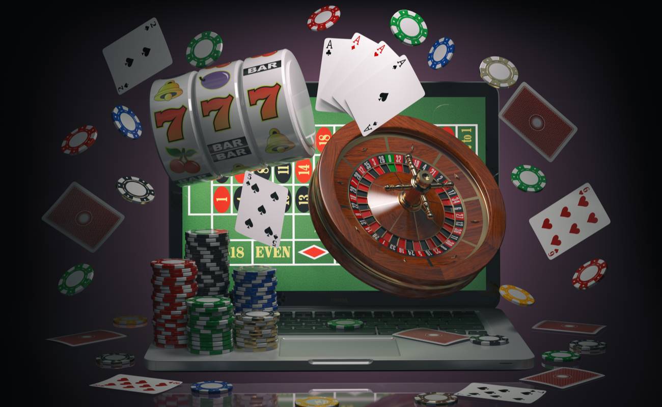 Poker chips, poker cards, spinning wheel and slot machine flying out and around a laptop.