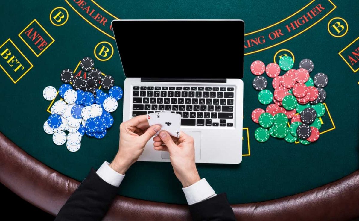 Hands holding 2 aces cards with a laptop on a poker table