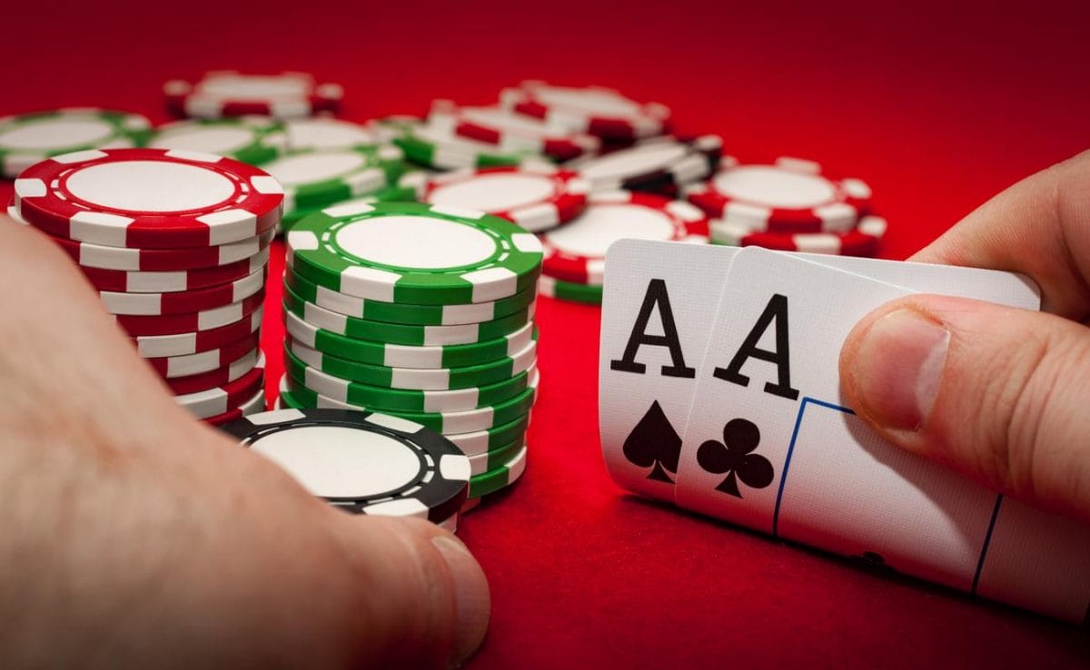 Hands holding 2 aces and poker chips on a red surface