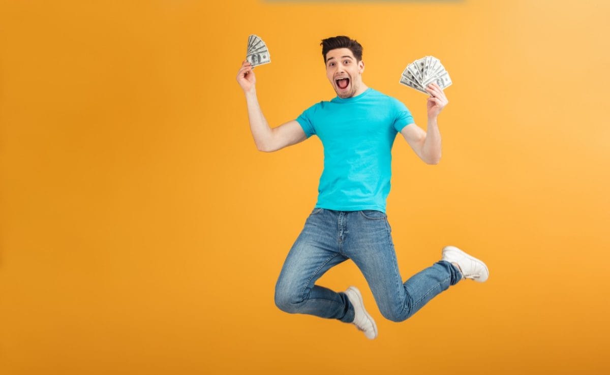 Man jumping holding money in both hands with orange background