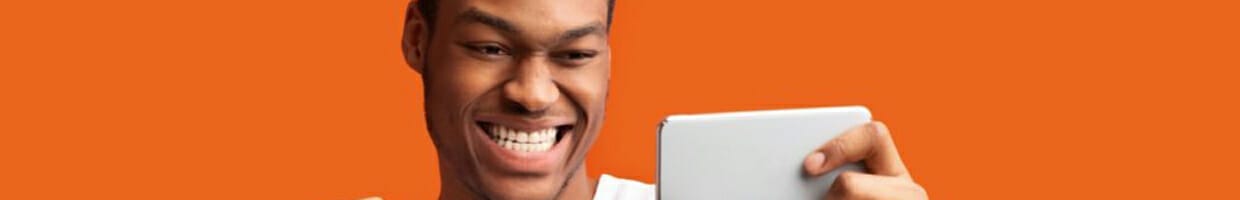 Man staring and smiling at mobile phone in front of orange background