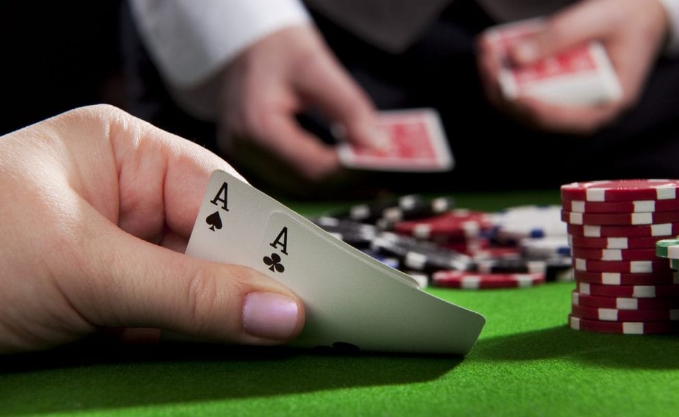 Close up of hand holding two aces with poker chips in background