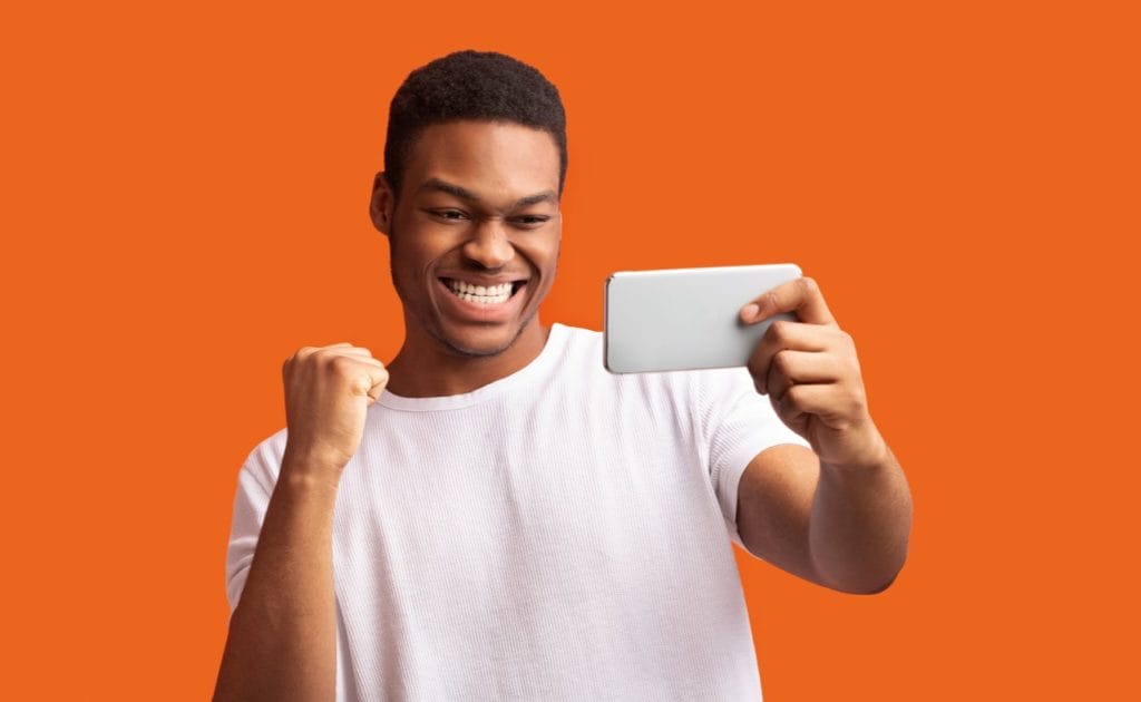 Man staring and smiling at mobile phone in front of orange background