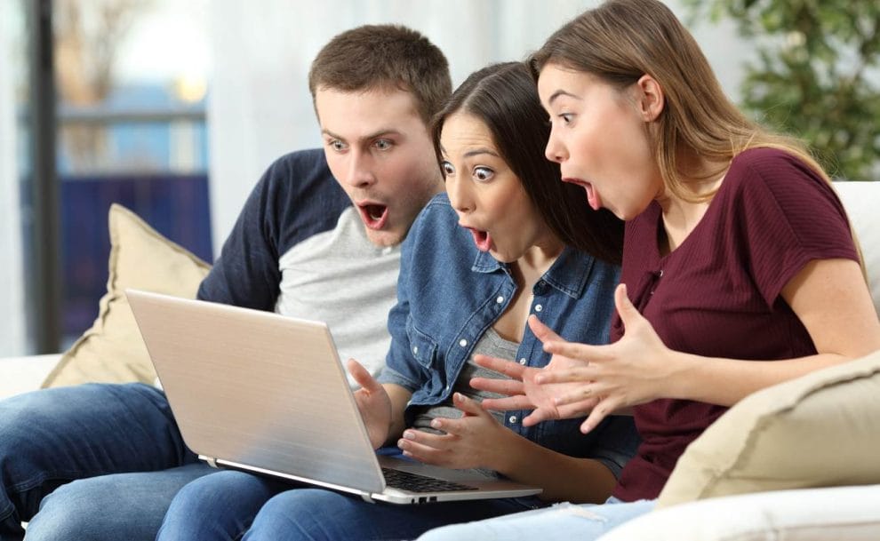 Three friends on computer on couch, amazed at online win