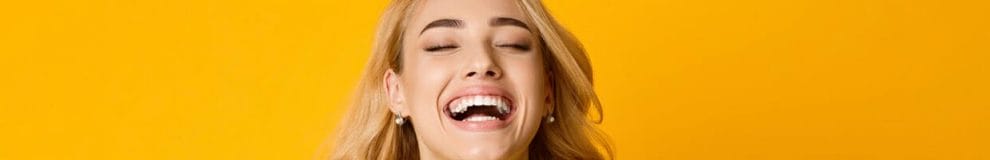 Woman laughing out loud standing against yellow background while wearing a yellow top