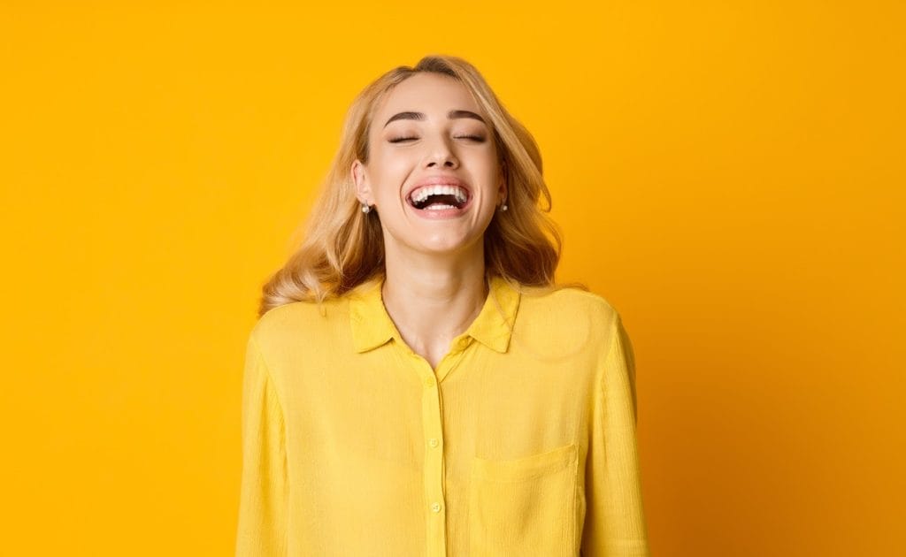 Woman laughing out loud standing against yellow background while wearing a yellow top
