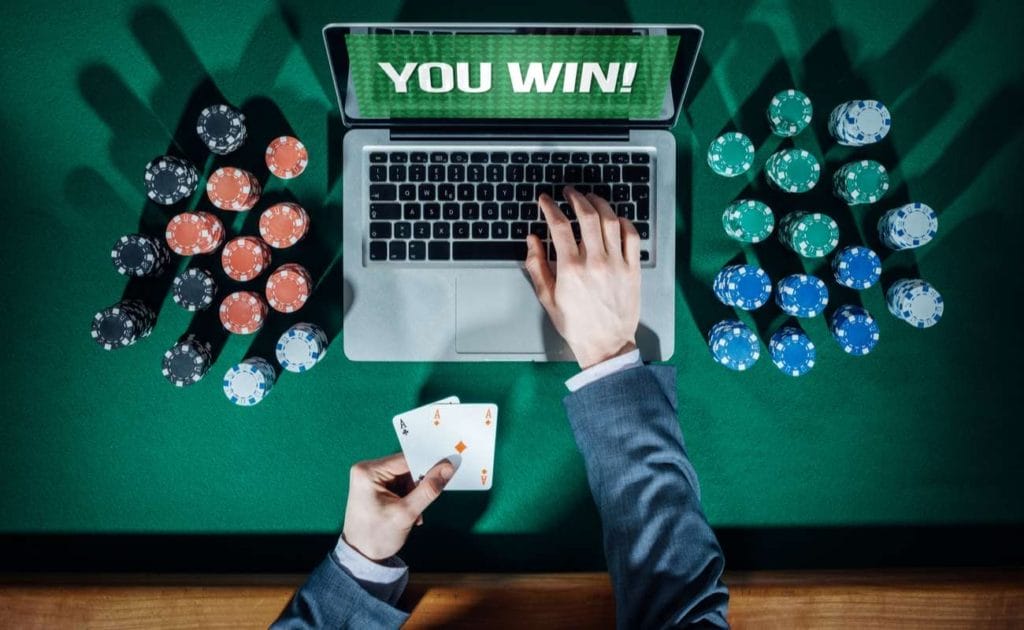 Top view of online player's hands holding cards with laptop and stack of chips on green table