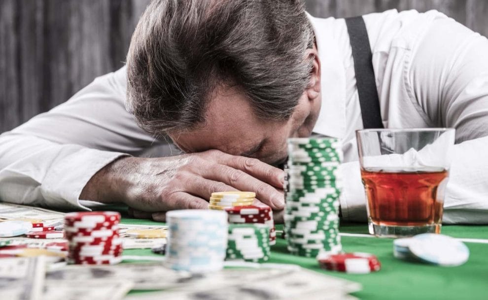 Depressed man leaning his head at poker table with money and gambling chips surrounding during poker loss