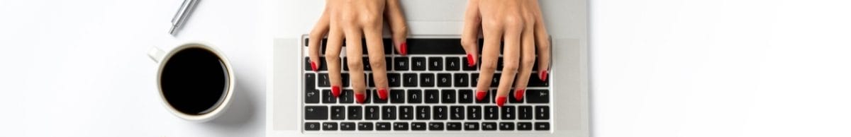 Female hands working on modern laptop, with coffee, a pen, and cactus next to the laptop