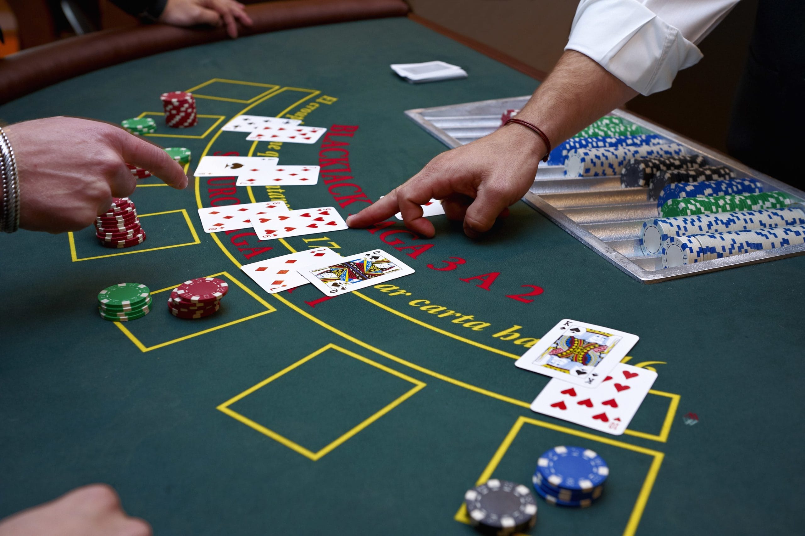 blackjack dealer and player pointing at card on blackjack table with chips