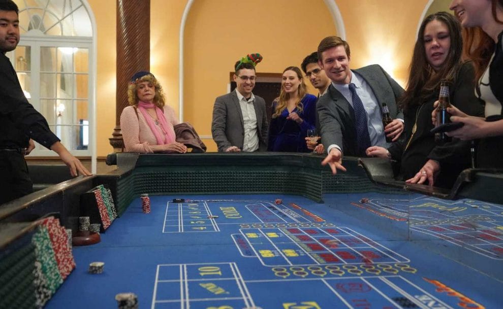Man rolls and throws the dice during a game of craps, while people around the table watch