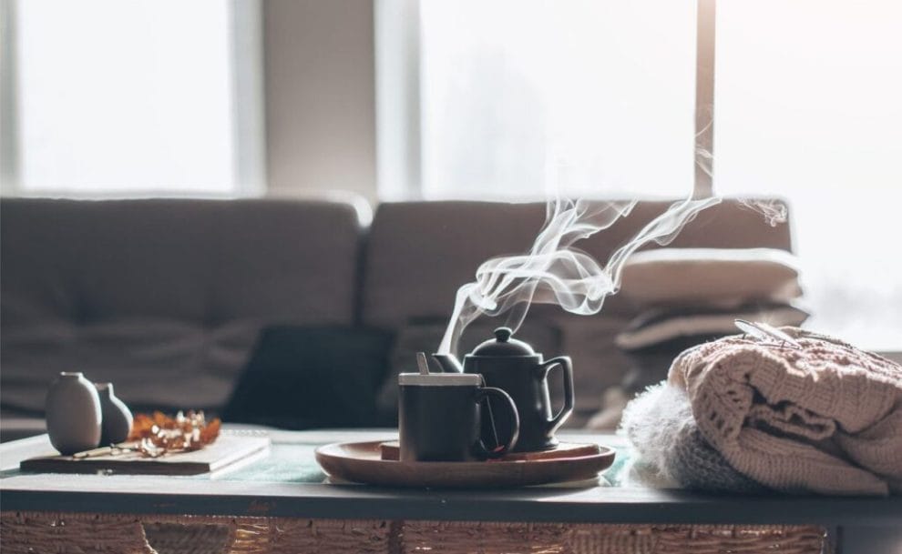 Sweaters and cup of tea with steam on a serving tray on a coffee table with couch in background