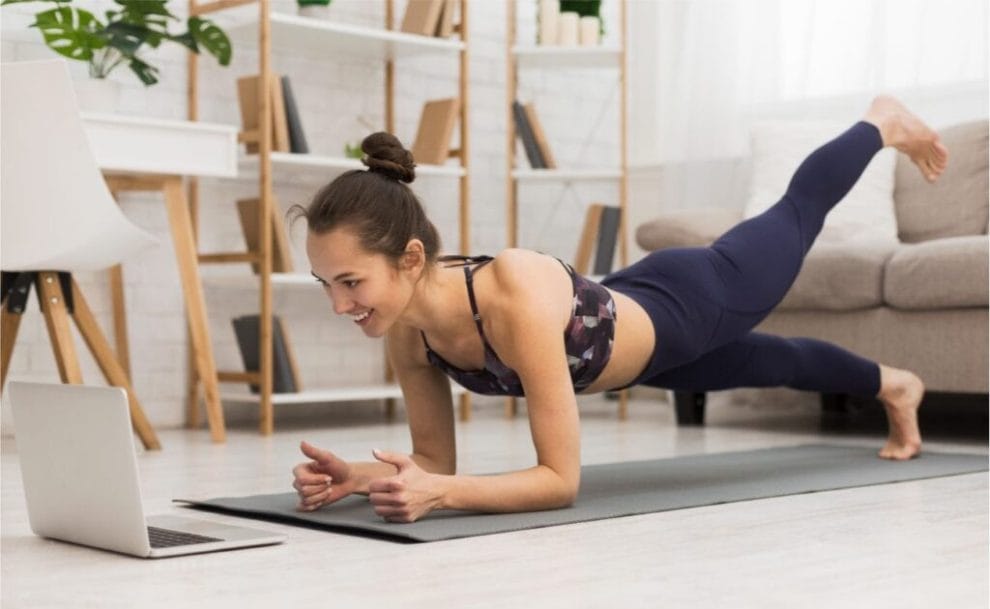  Fit woman doing yoga plank and watching online tutorials on laptop in living room