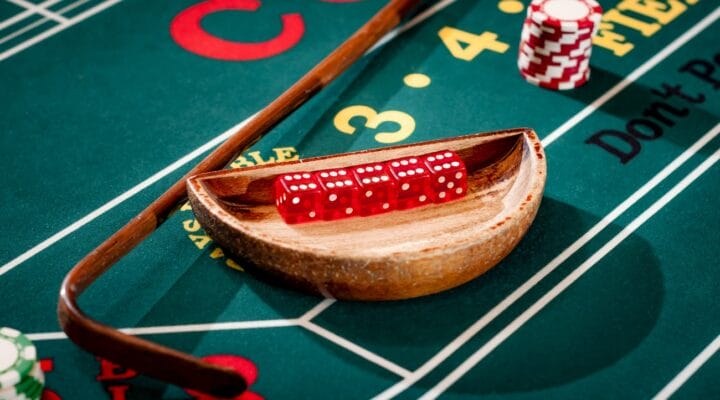 Full set of 5 dice in a wooden bowl next to the stick on a craps table with stacks of casino chip around