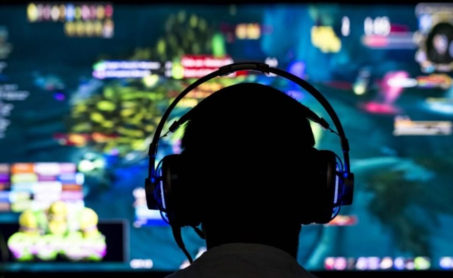 Gamer wearing headphones in front of large screen playing games online