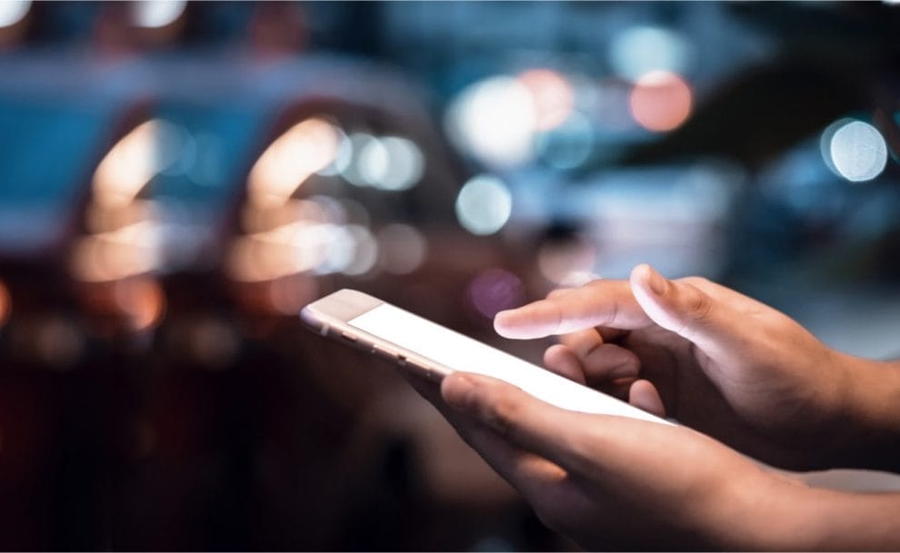 Close-up image of male hands using smartphone at night on a city shopping street