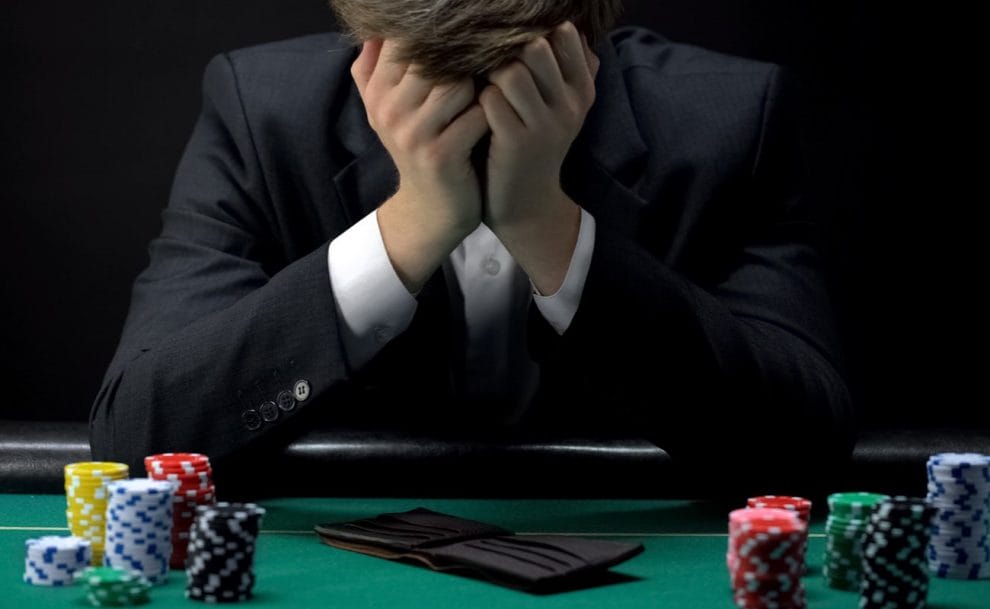 A man sits at a poker table with an empty wallet and his head in his hands