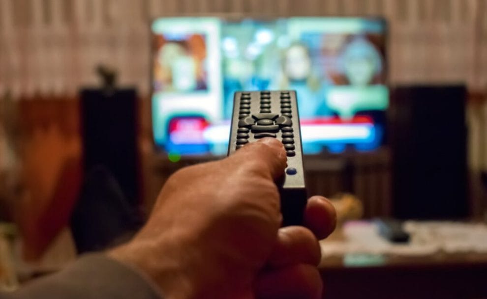 A thumb on a remote button with TV in the background