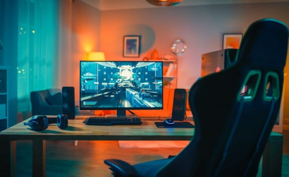 Computer gamer rig with monitor stands on table in modern room lit with neon light.