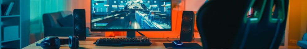 Computer gamer rig with monitor stands on table in modern room lit with neon light.

