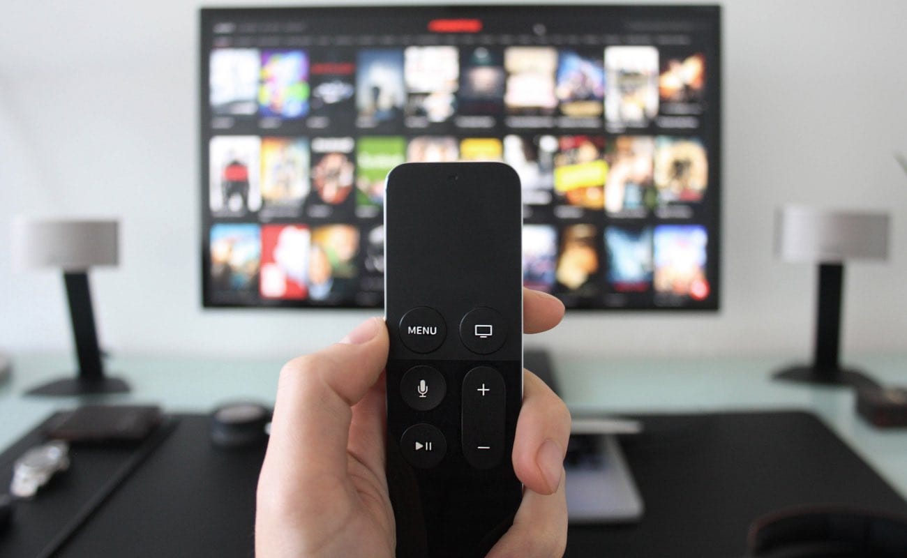 Hand holding a TV remote while watching shows on a streaming service on Television.