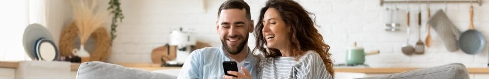 Happy couple sitting on the couch playing casino games on a smartphone