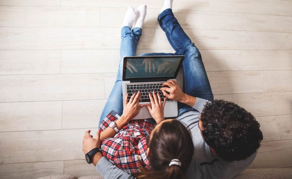 Couple sitting on the floor looking at a laptop screen