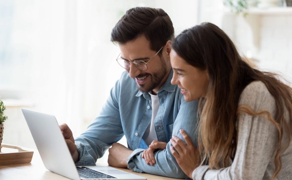 Smiling couple sitting at a table looking at laptop screen