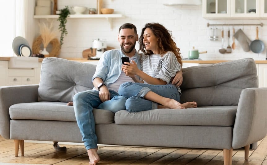 Happy couple sitting on the couch playing casino games on a smartphone