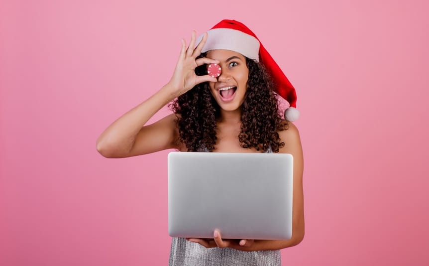 Woman with casino poker chip wearing holiday Santa hat isolated over pink background