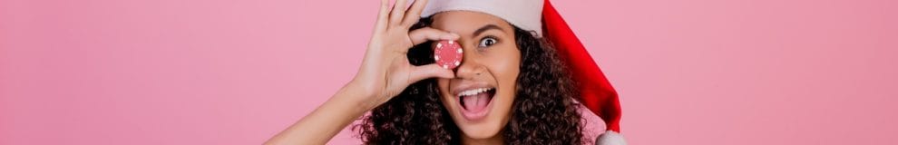 Woman with casino poker chip wearing holiday Santa hat and dress isolated over pink background.