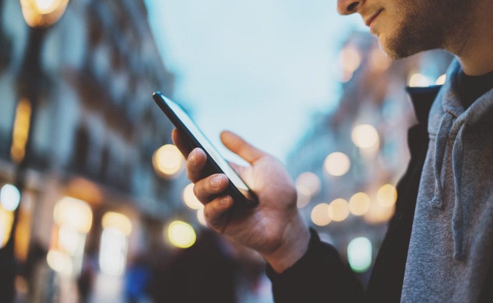 Side view of man using smartphone at night with city street in the background
