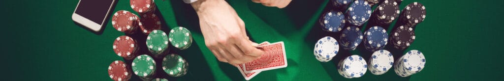 Hands holding cards with casino chips and a smartphone on a green casino table.