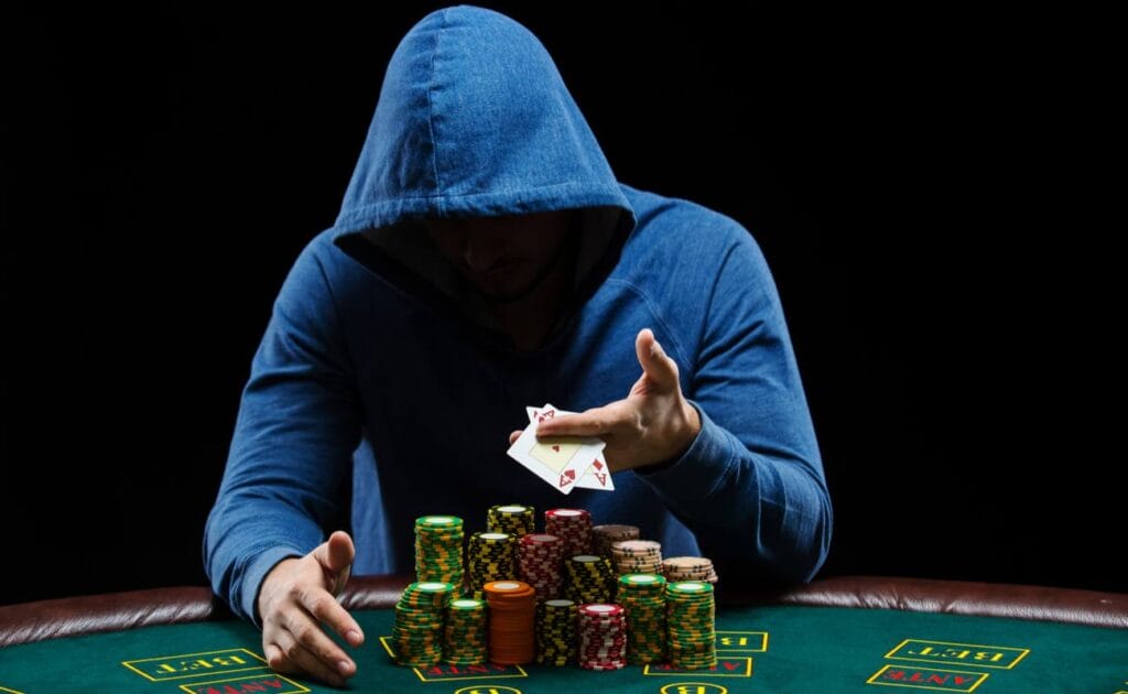 Man in a blue hoodie at a casino table showing a pair of aces with a large stack of casino chips.