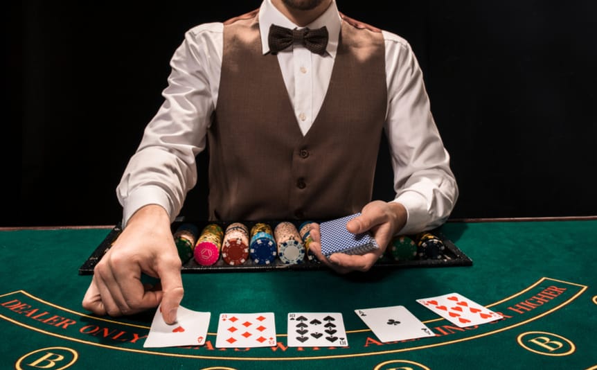A dealer places cards face up on a green felt casino table.