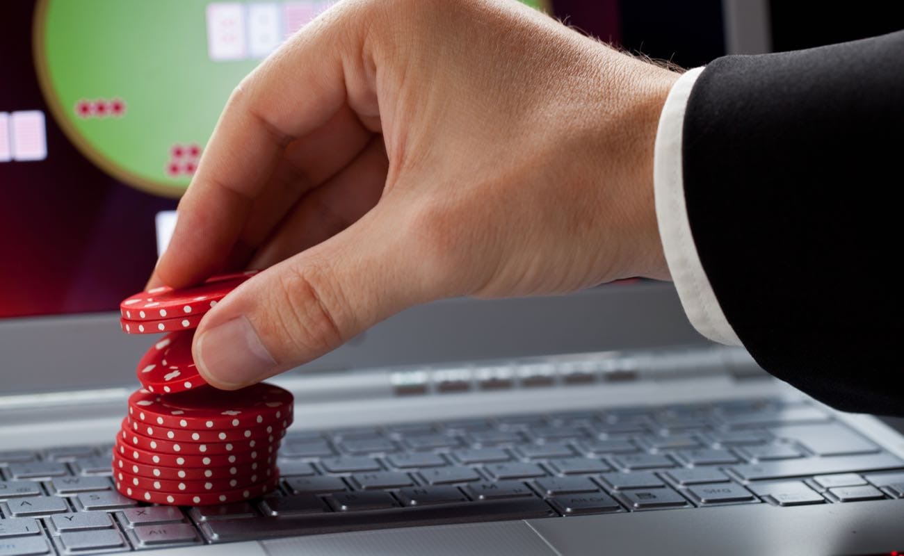 Online poker player stacking red casino chips on a laptop that is showing an online casino.