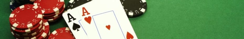 A pair of aces lies against a stack of casino chips on a green felt casino table.