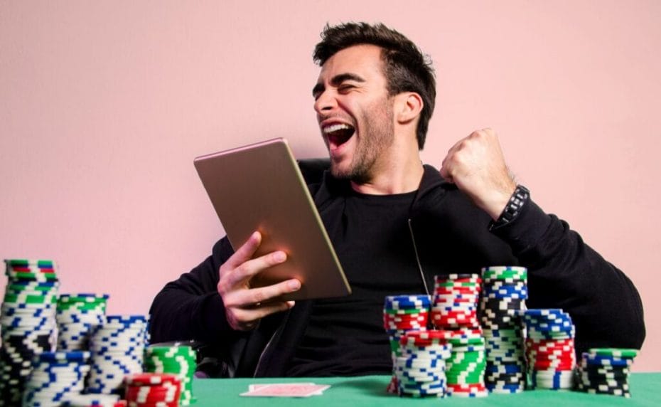 A happy poker player sitting behind stacks of casino chips wins a game of online poker on his tablet.