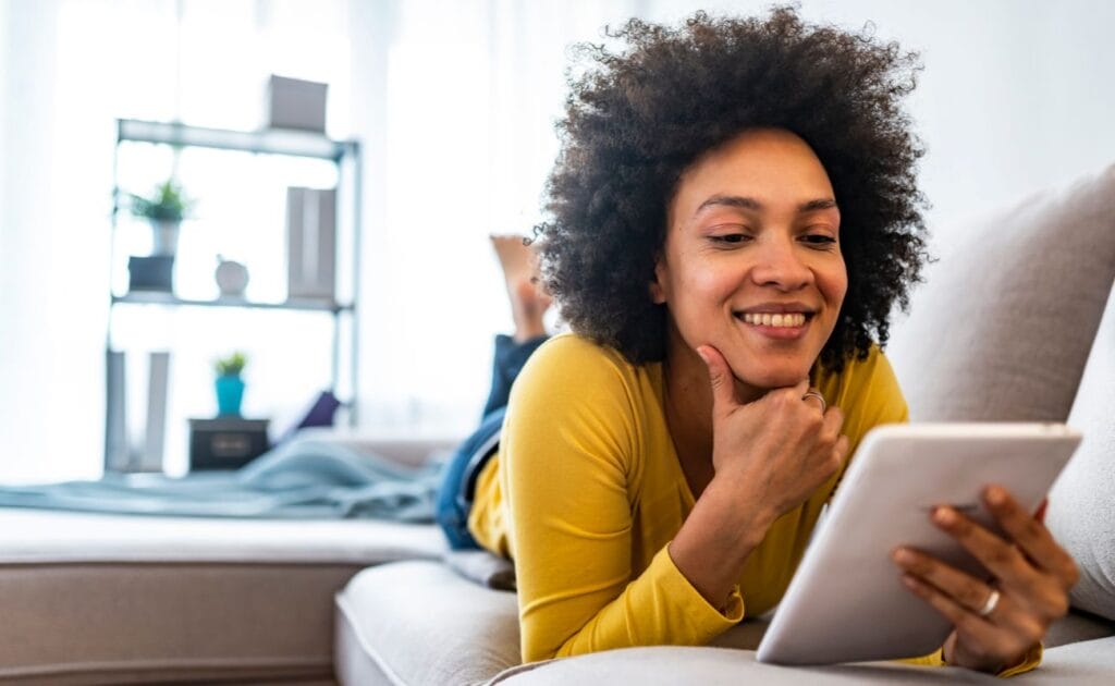 A young woman plays online bingo while lying on her couch.