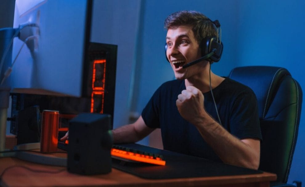 A young man celebrates while sitting at his gaming PC.