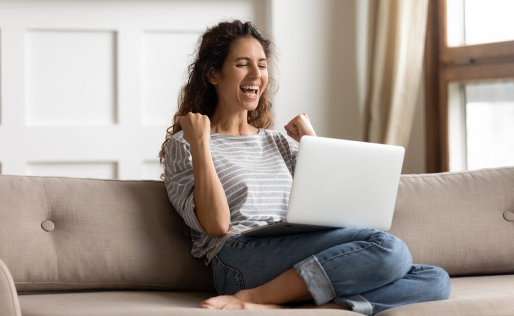 A woman sitting on a couch celebrates her online casino win.