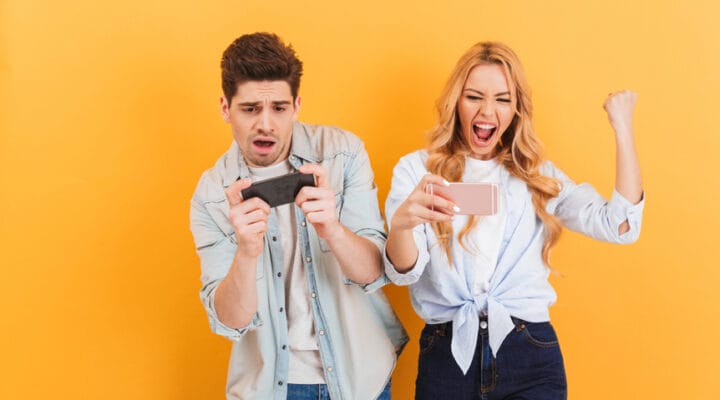 A young man and woman cheering and celebrating while playing mobile games.