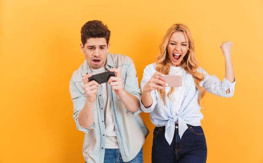 A young man and woman cheering and celebrating while playing mobile games.