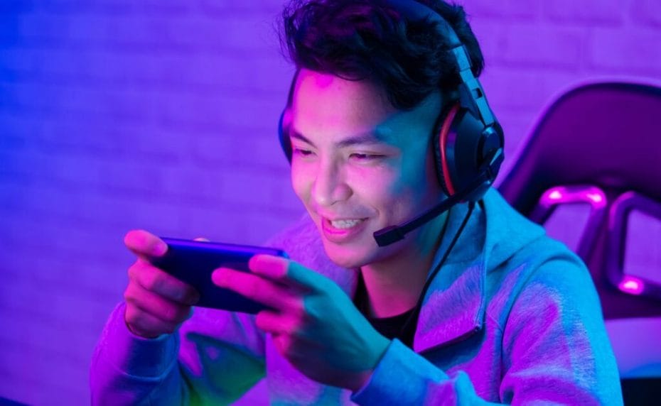 A gamer smiling and playing mobile games with purple lights.