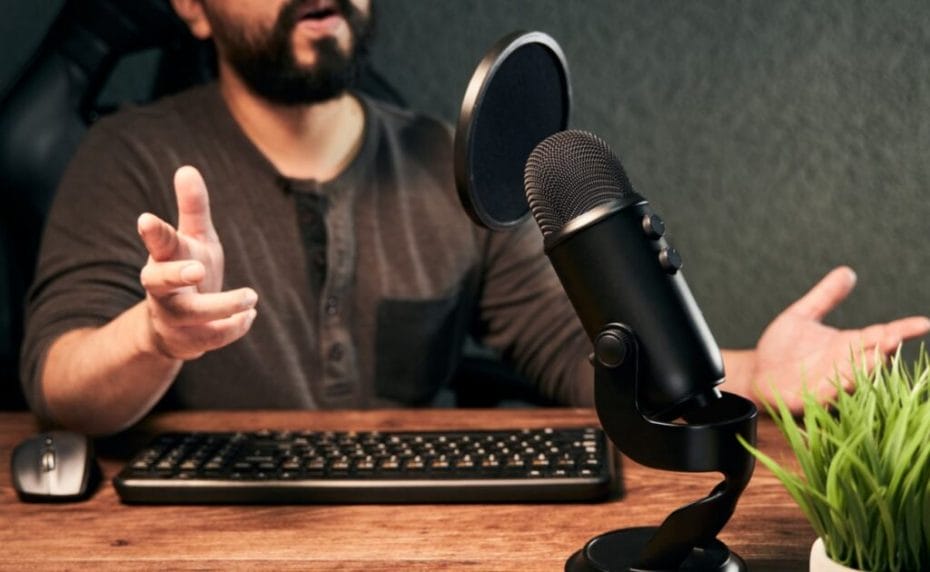 A man speaks into a dedicated desktop microphone with a pop filter.
