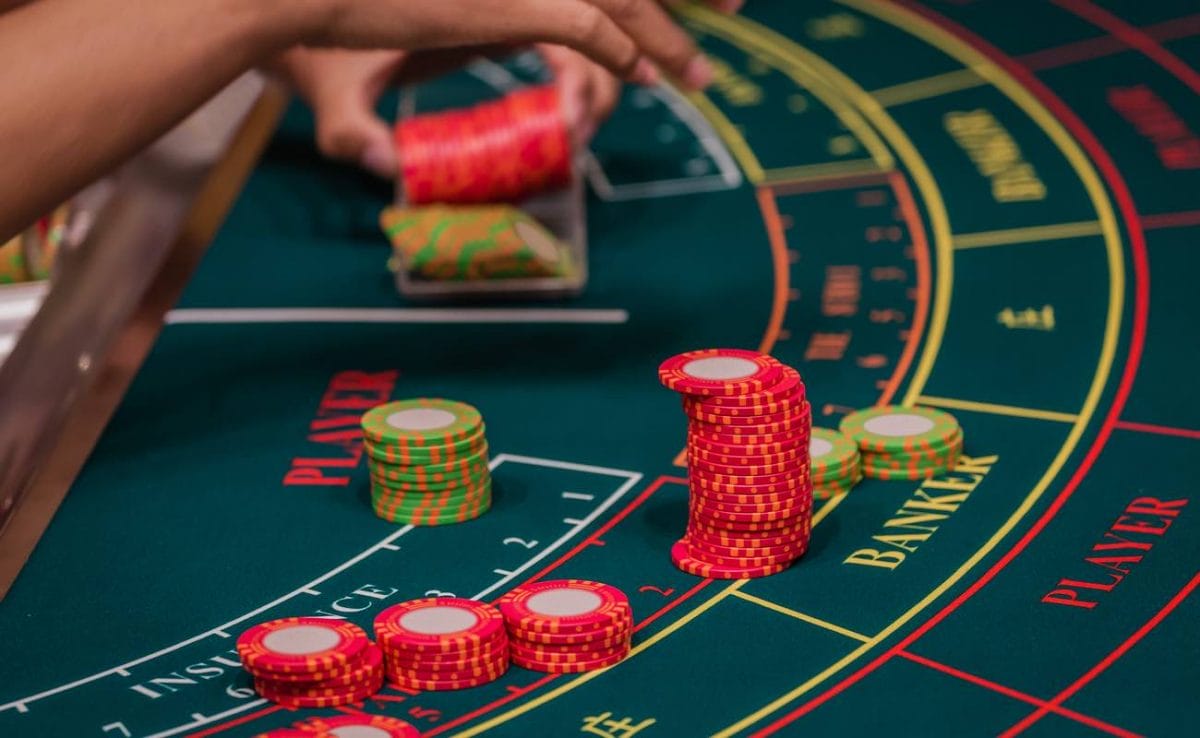 The hand of a dealer organizing red and green chips on a baccarat table.