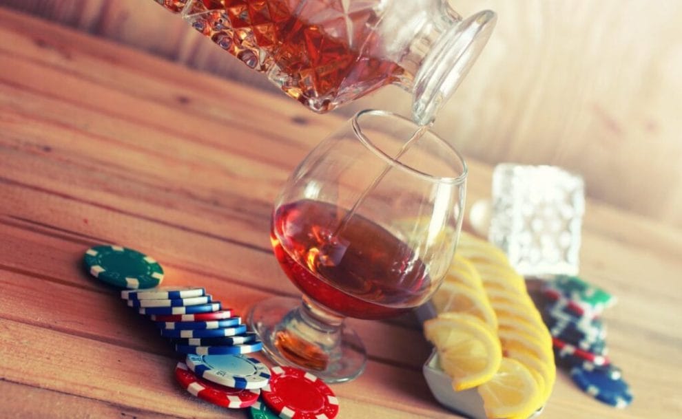 A drink being poured from a decanter into a glass with lemon slices and poker chips.